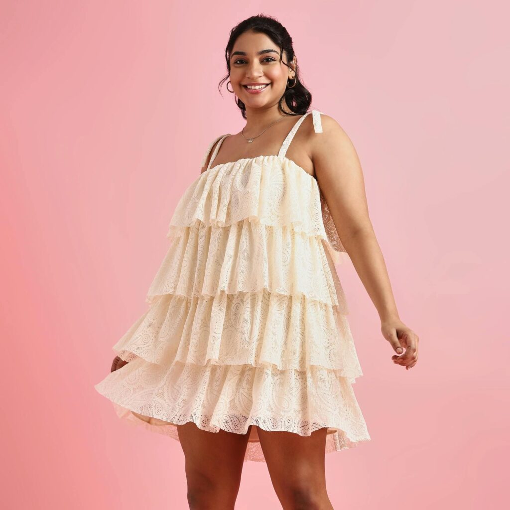 Smiling woman wearing a layered cream dress against a pink backdrop.
